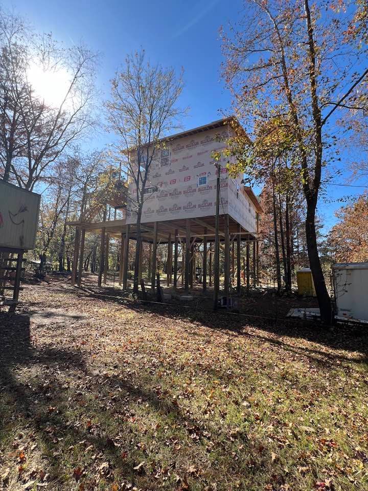 A raised wooden structure, resembling a house, under construction in a wooded area.