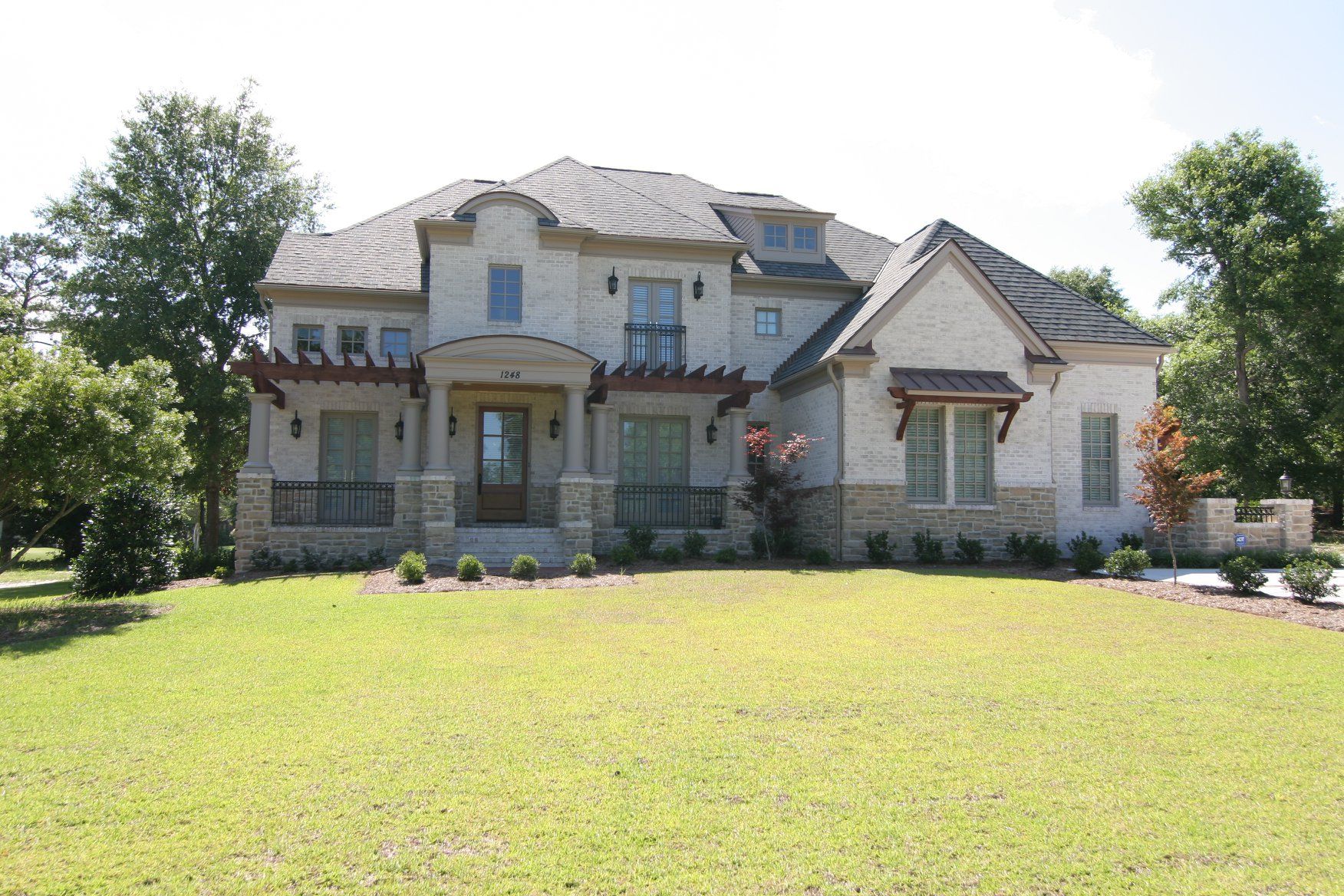 Large two-story stone house with a lawn, trees, and a pergola above the front door.