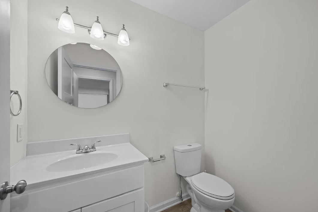 White bathroom with toilet, sink, mirror, and light fixture.