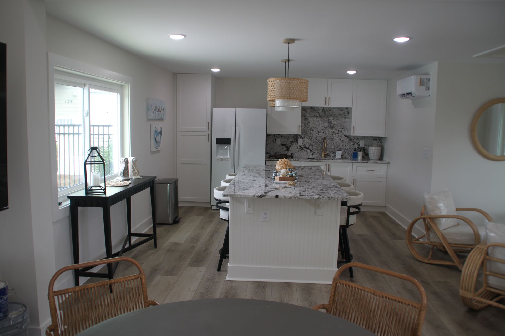 Bright kitchen with white cabinets, island, and appliances. Woven chairs surround a round table.