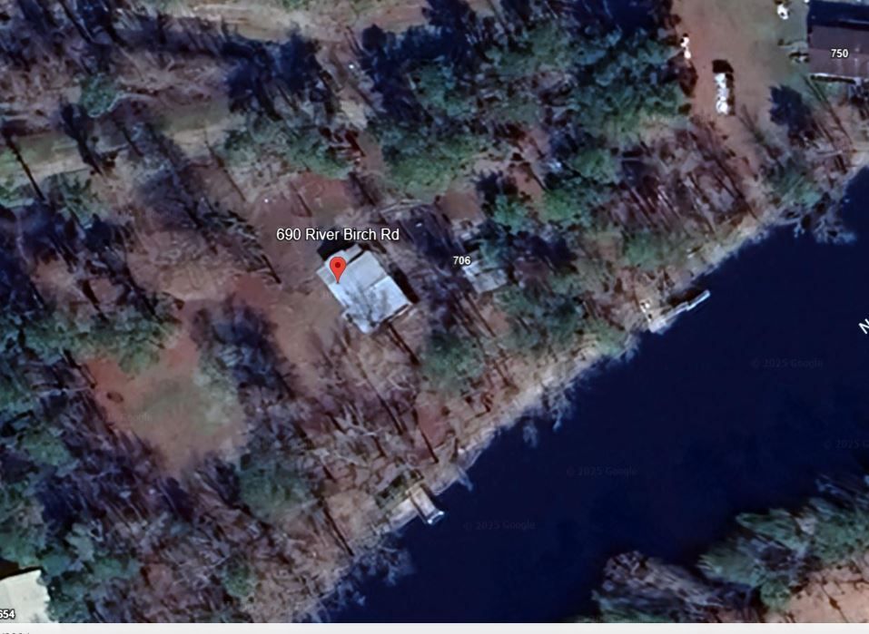 Aerial view of a building with a red marker, next to a body of water and surrounded by trees.