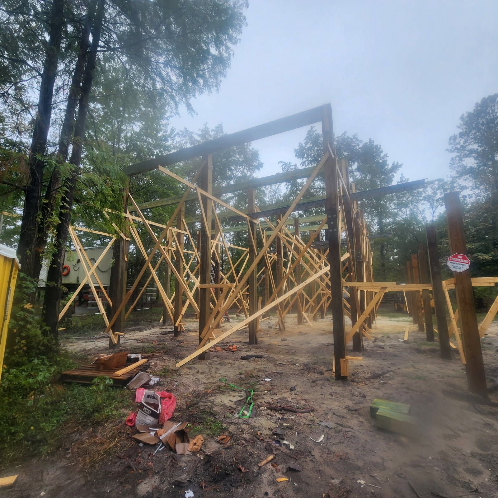 Wooden frame of a building under construction amidst trees on a rainy day.