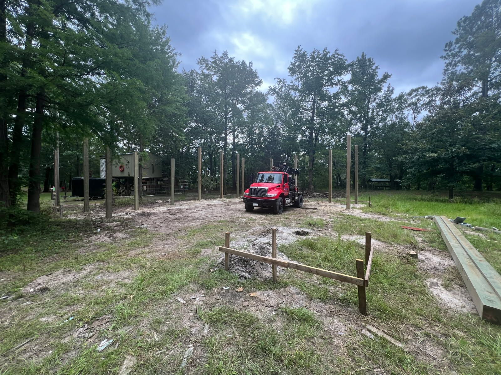Construction site with wooden posts and a red truck, under a cloudy sky.