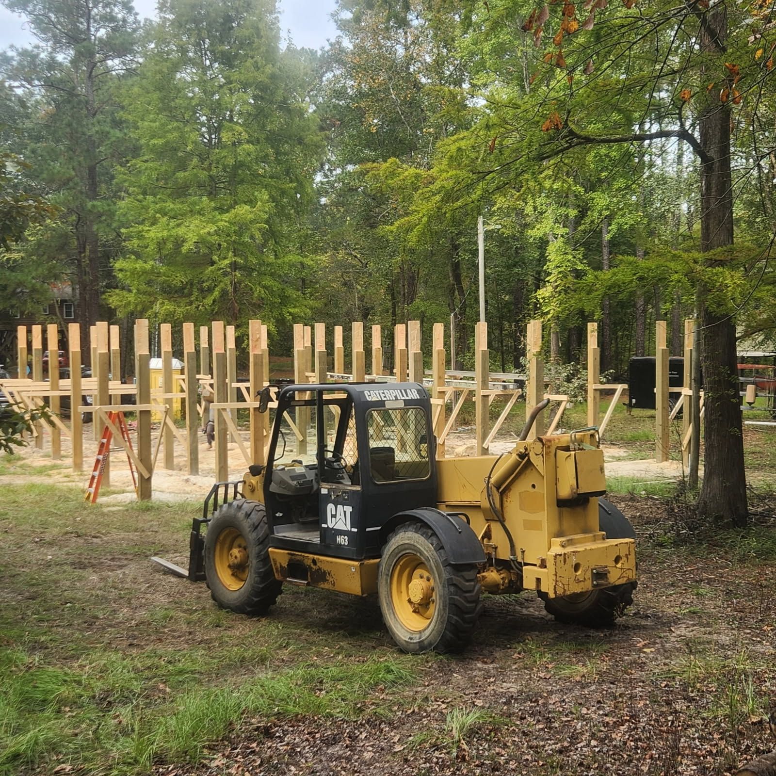 Yellow construction forklift in a grassy area with a partially built wooden structure.