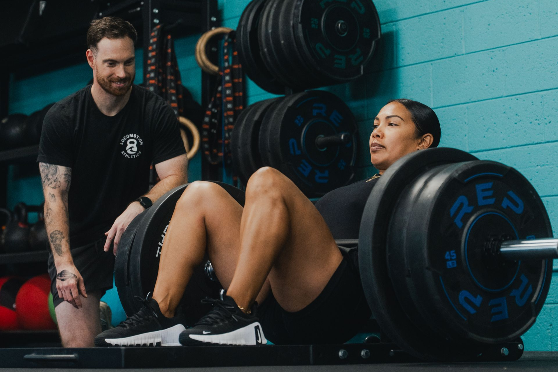 A man is helping a woman squat with a barbell in a gym