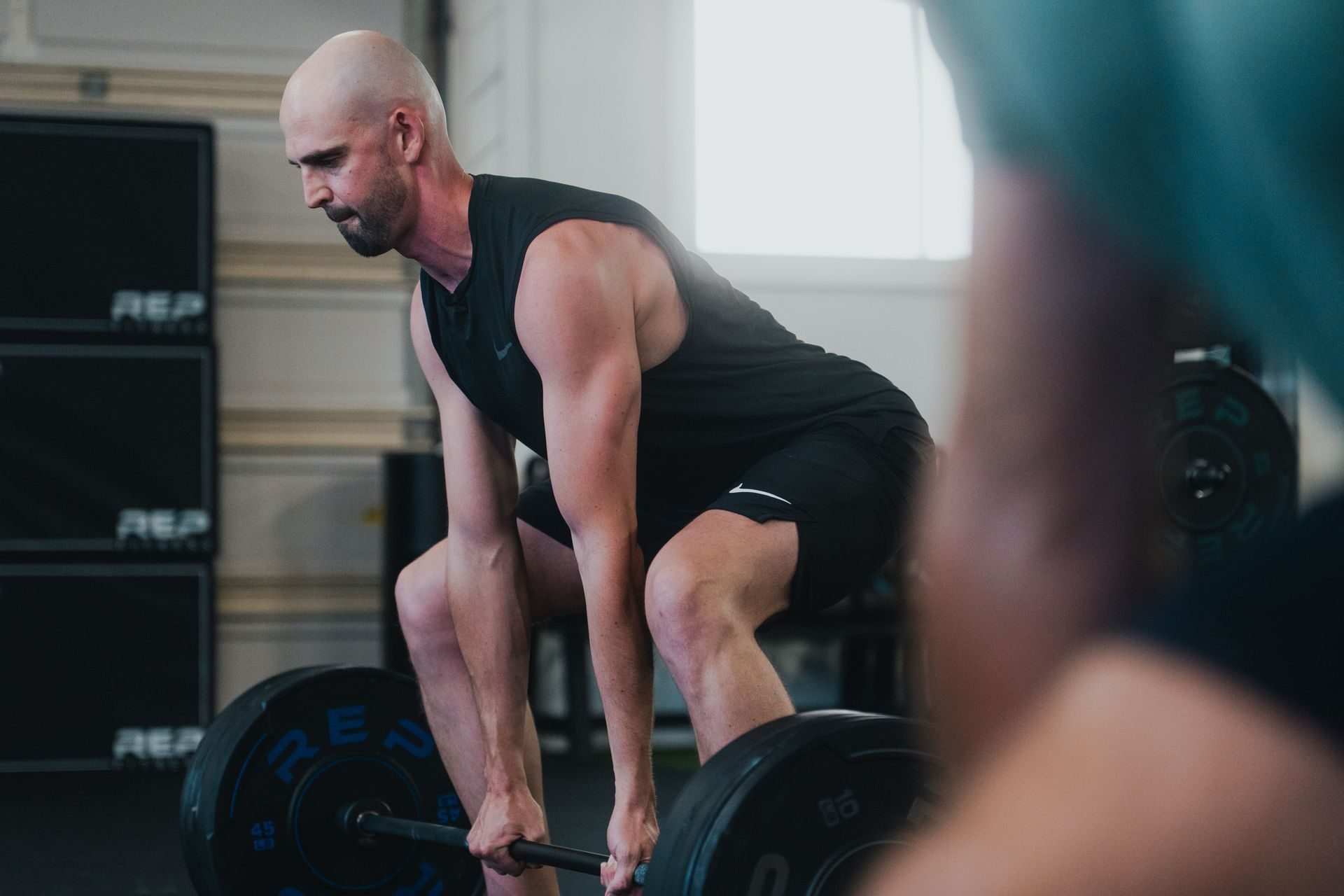 A man is squatting down to lift a barbell in a gym.