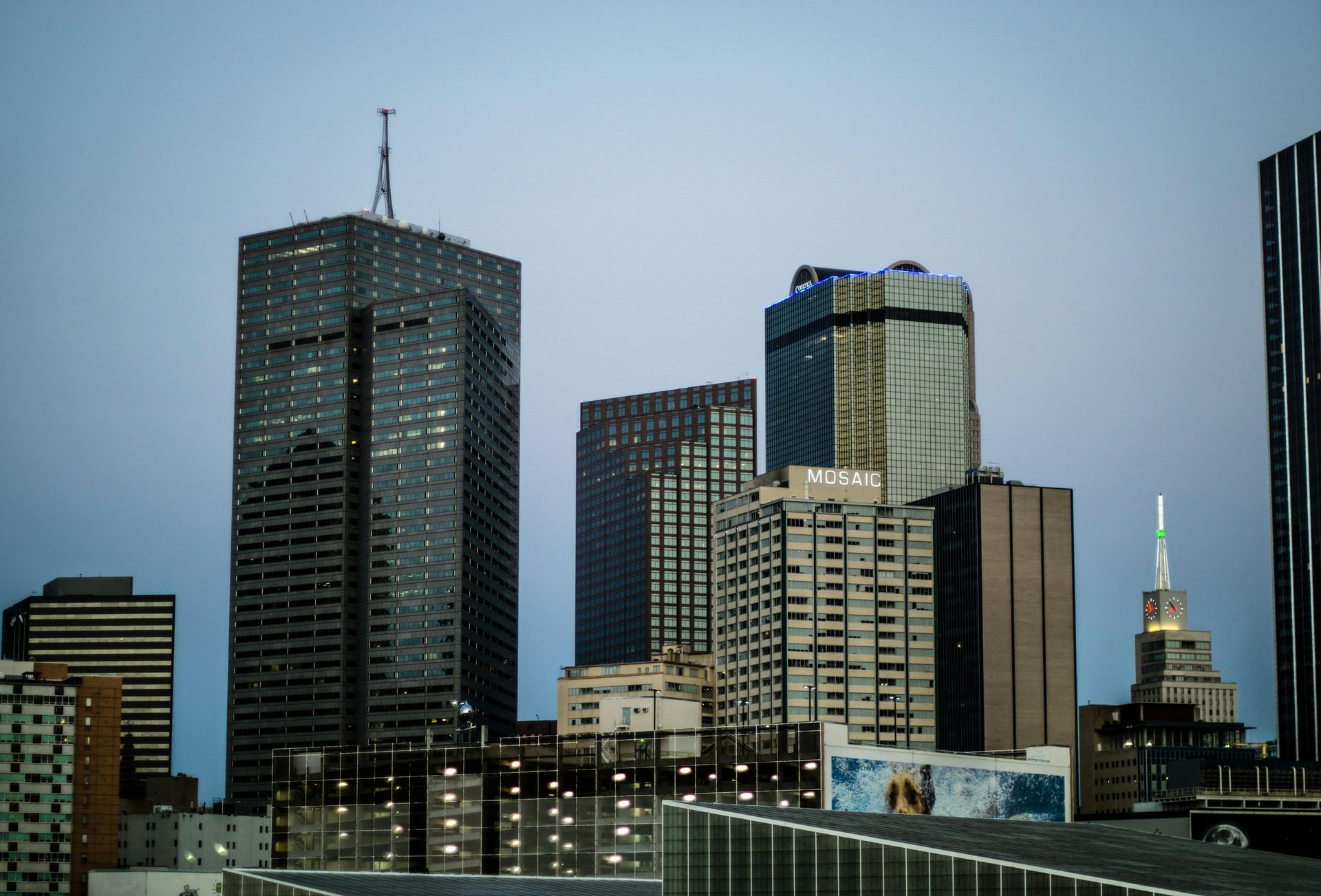 A cluster of modern skyscrapers in a city skyline at twilight with a mix of dark, light, and reflective glass facades.
