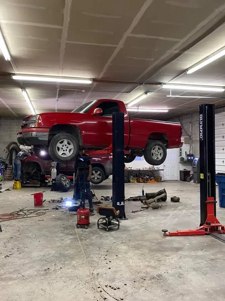 Red pickup truck lifted on a car lift in an auto repair shop with tools and equipment nearby