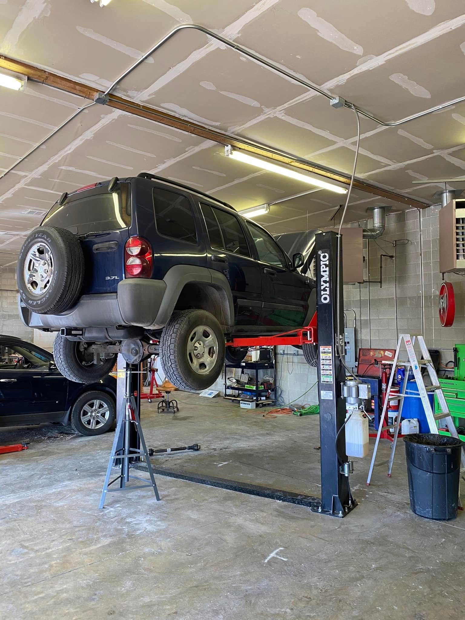 Black SUV raised on a lift in an auto repair garage, with tools and equipment nearby.