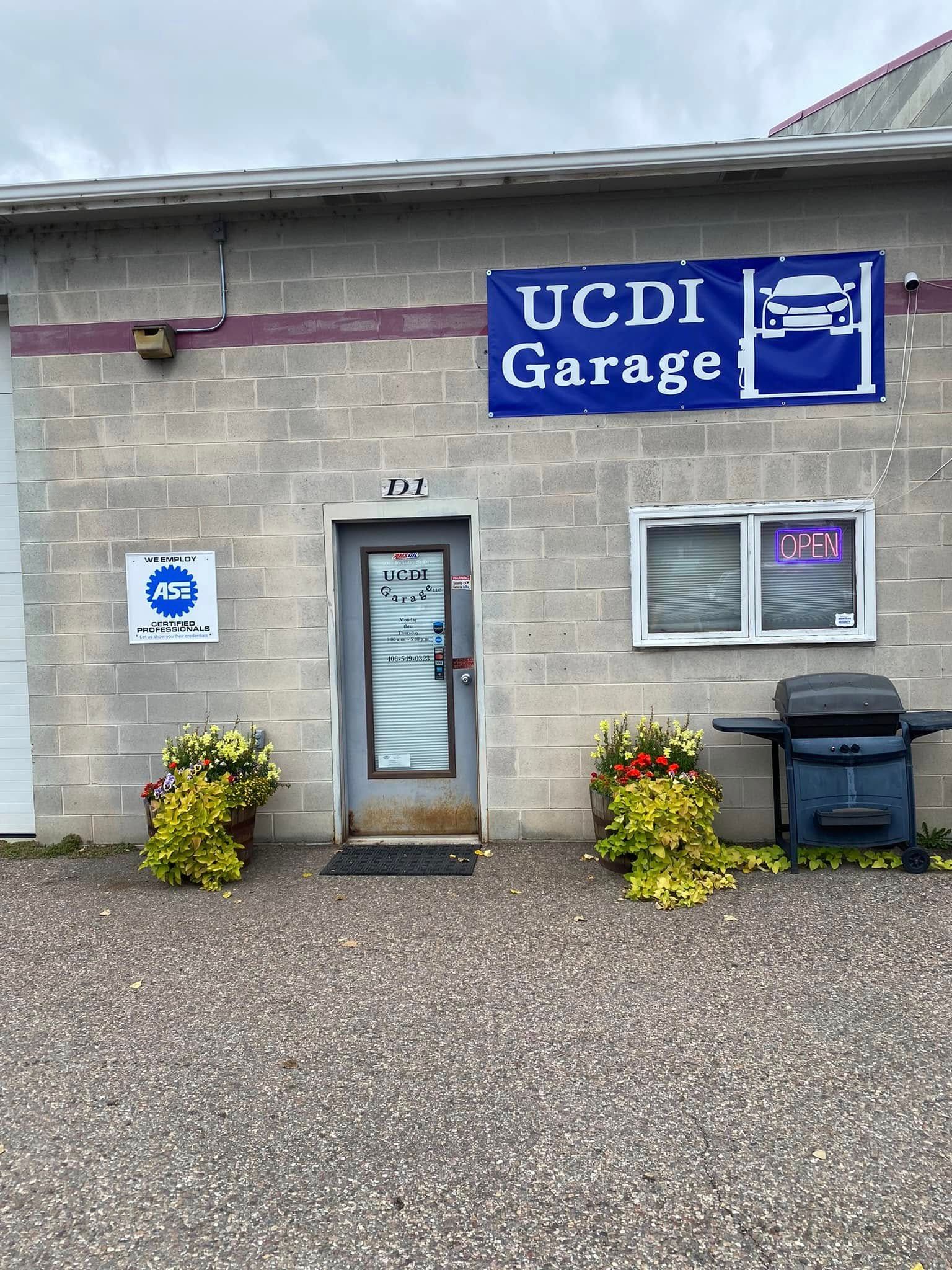 UCD Garage entrance on a stone building with blue sign, door, window, plants, and trash bins