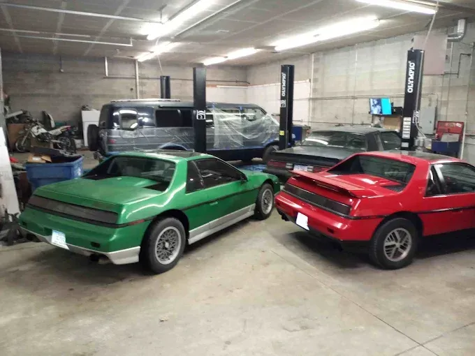 Two classic sports cars, one green and one red, parked inside a garage workshop.