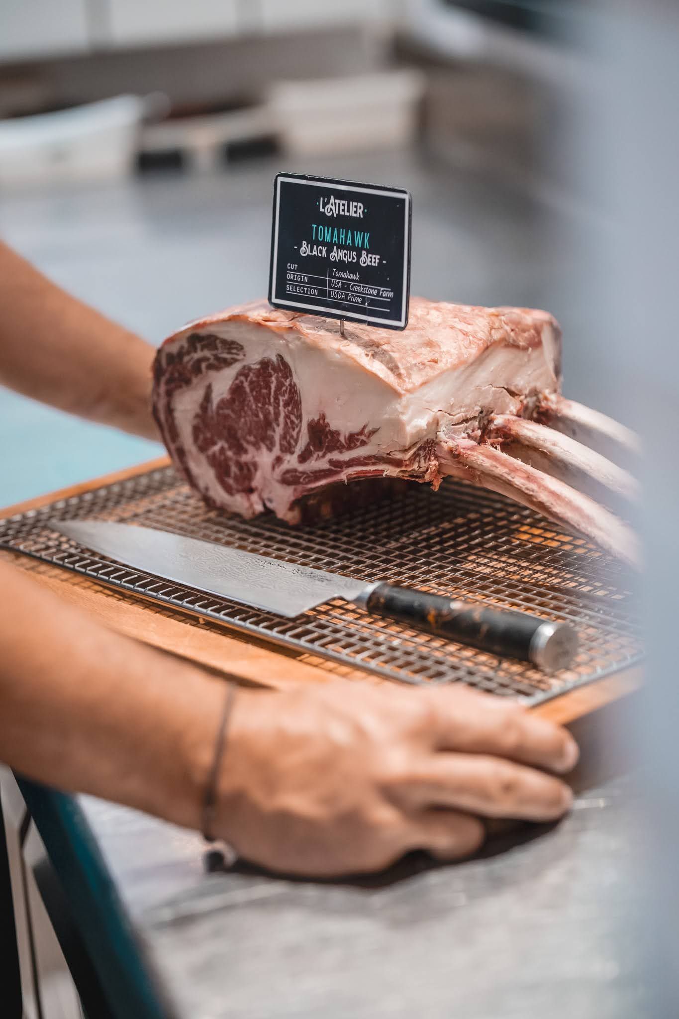 Cured meat slice on a grill rack with a small label, while a person’s hands hold the rack.