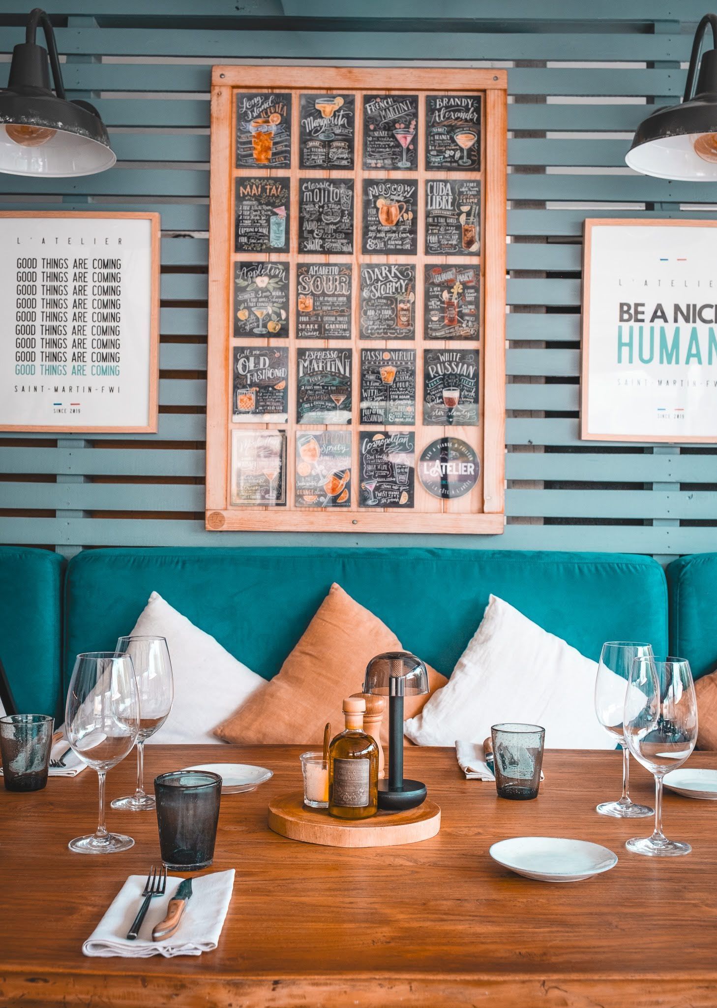 Cozy restaurant table with teal wall, framed art, wine glasses, and tan pillows on a wooden banquette