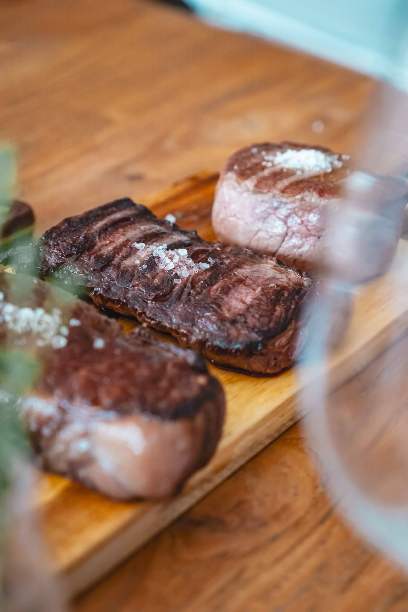 Seared steaks on a wooden board, viewed through a glass, in a kitchen setting