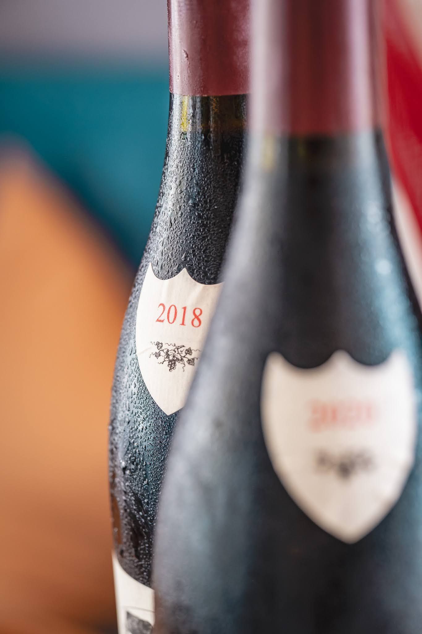Close-up of two dark wine bottles with cream labels and red caps