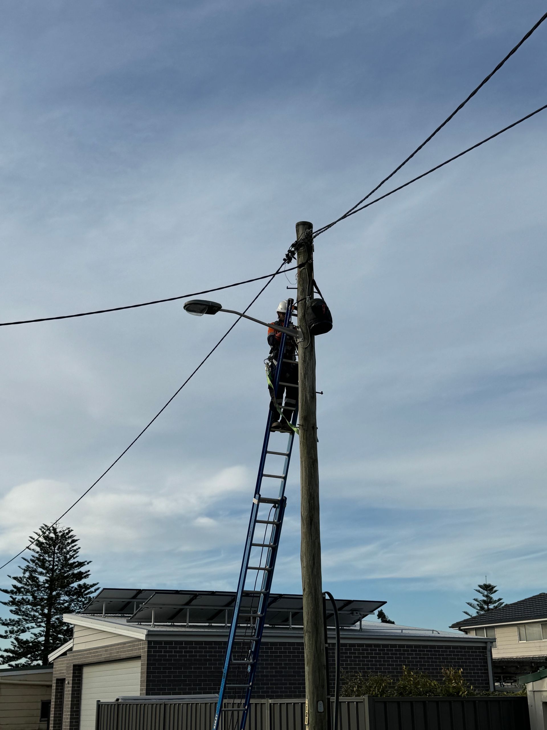 Utility worker on a ladder, working on a utility pole with power lines — Powered By JBES In Maitland, NSW