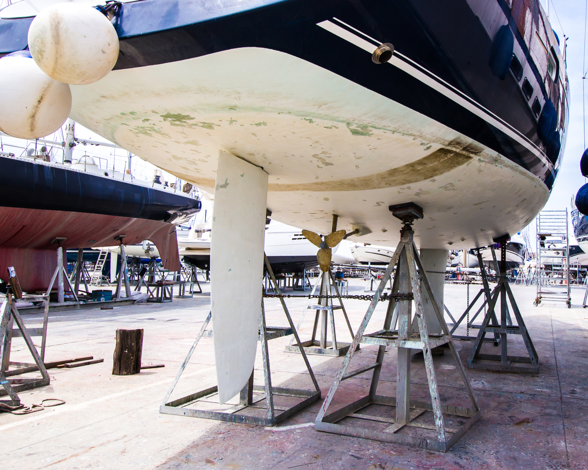 Sailboat in dry dock, supported by metal stands, with visible keel and propeller.