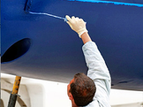 Person in white work clothes paints a blue surface with a roller.