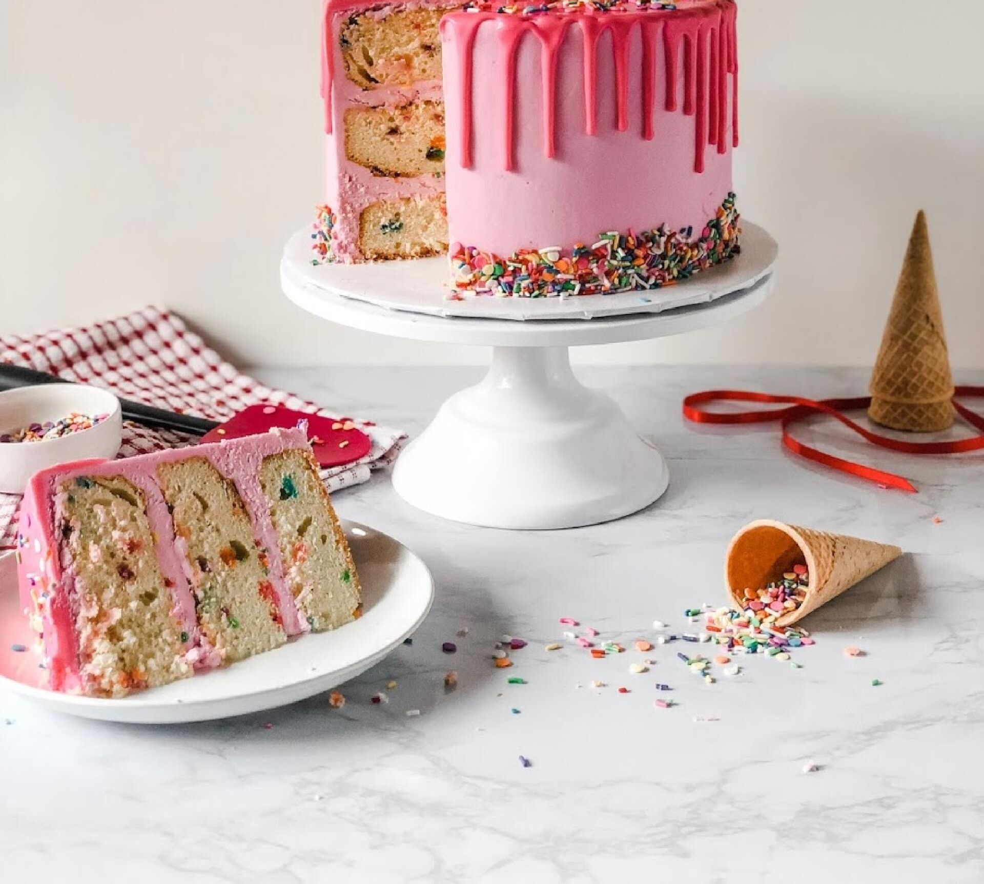 Pink layered cake with dripping icing displayed beside neatly arranged sliced pieces