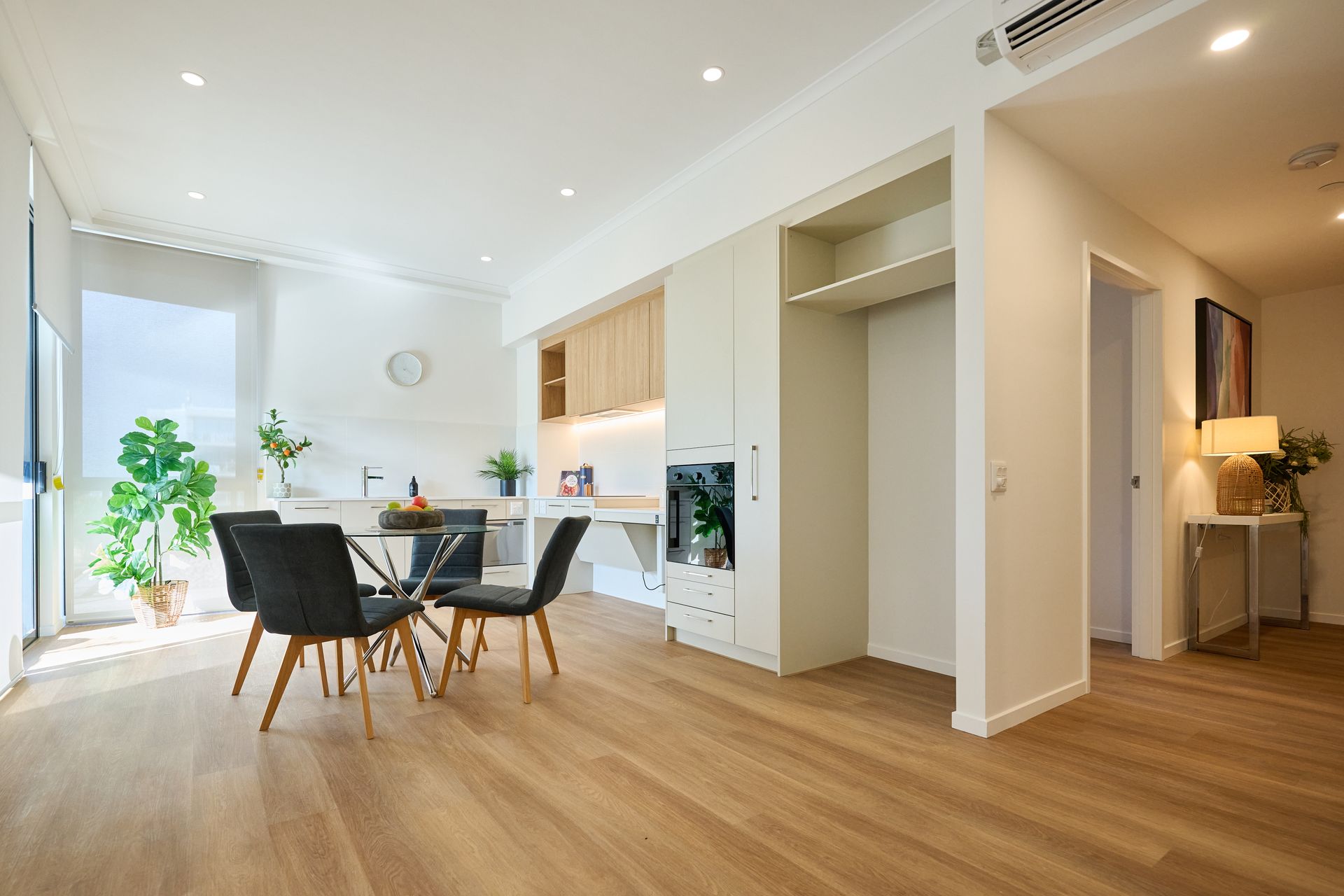 Bright modern dining room with round table, black chairs, wood floors, and large windows.
