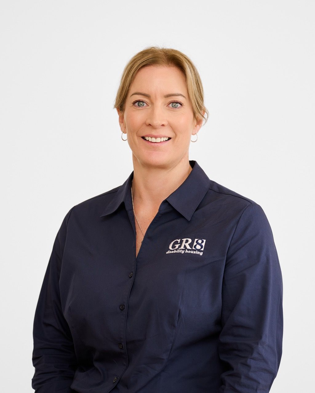 A woman is wearing a blue polo shirt and smiling.