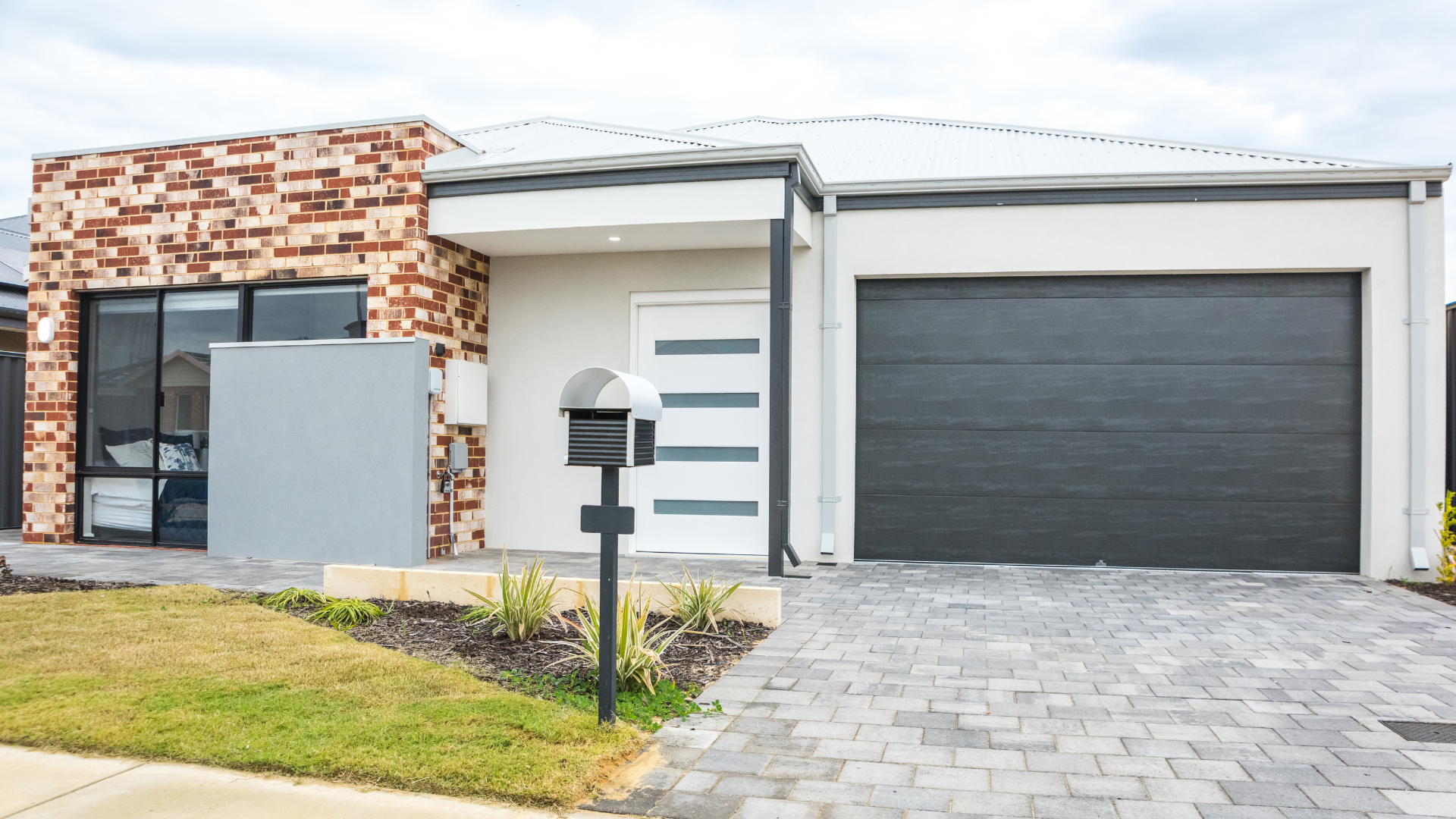 Modern single-story house exterior with white and brick facade, dark garage door, and paved driveway