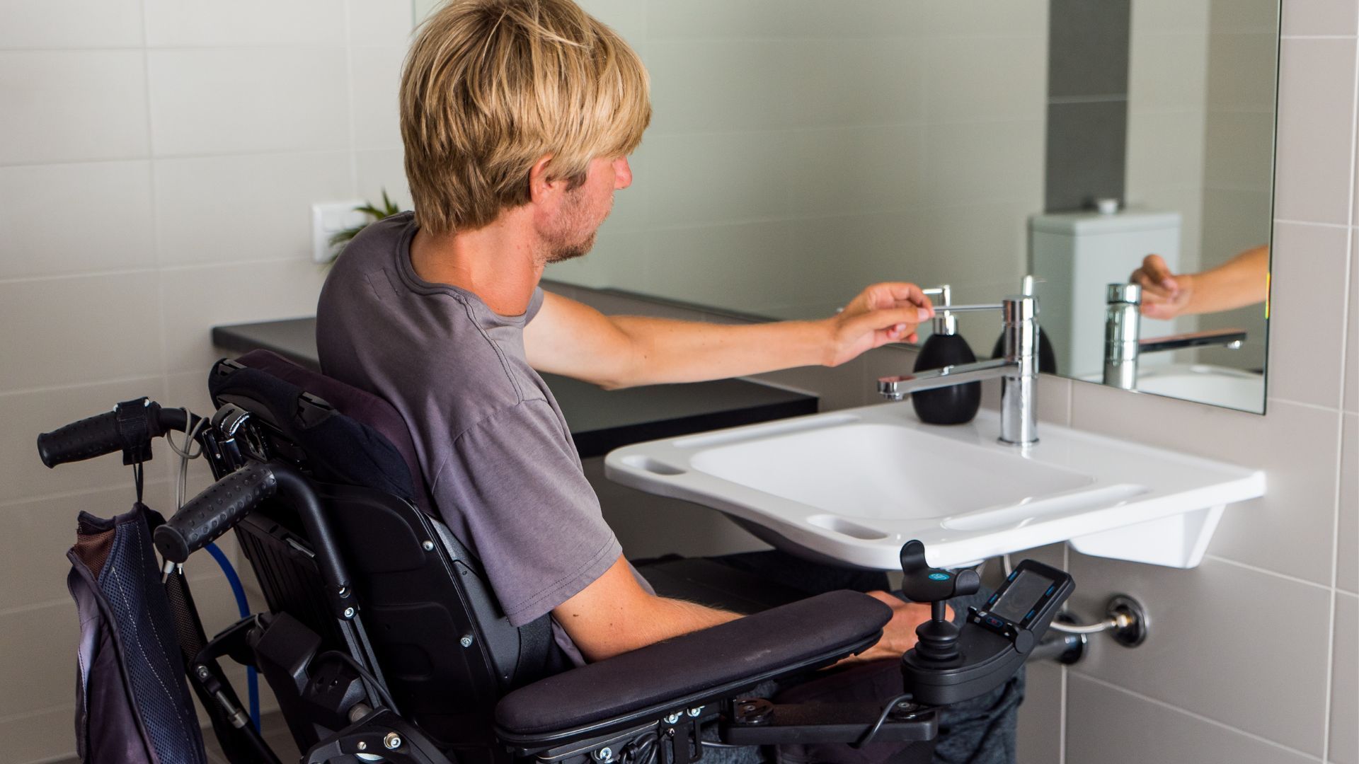 Man in wheelchair using a low sink in an accessible bathroom.