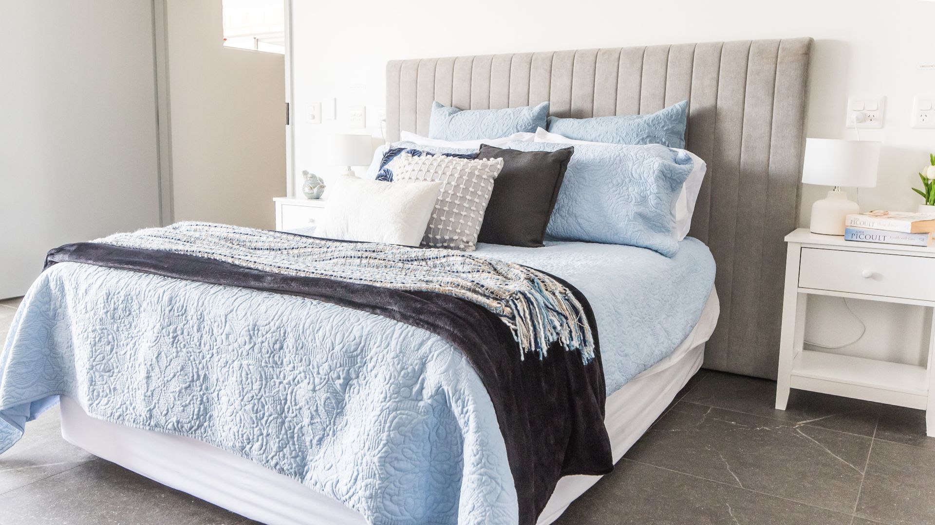 Bedroom with light blue bedding, gray headboard, and white nightstand.
