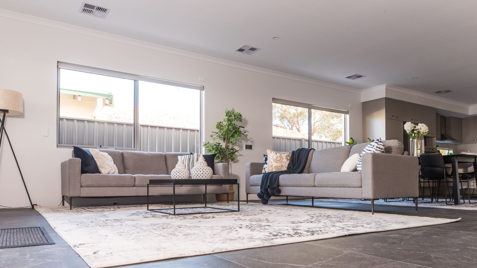 A modern living room with two gray sofas, a white rug, and large windows.