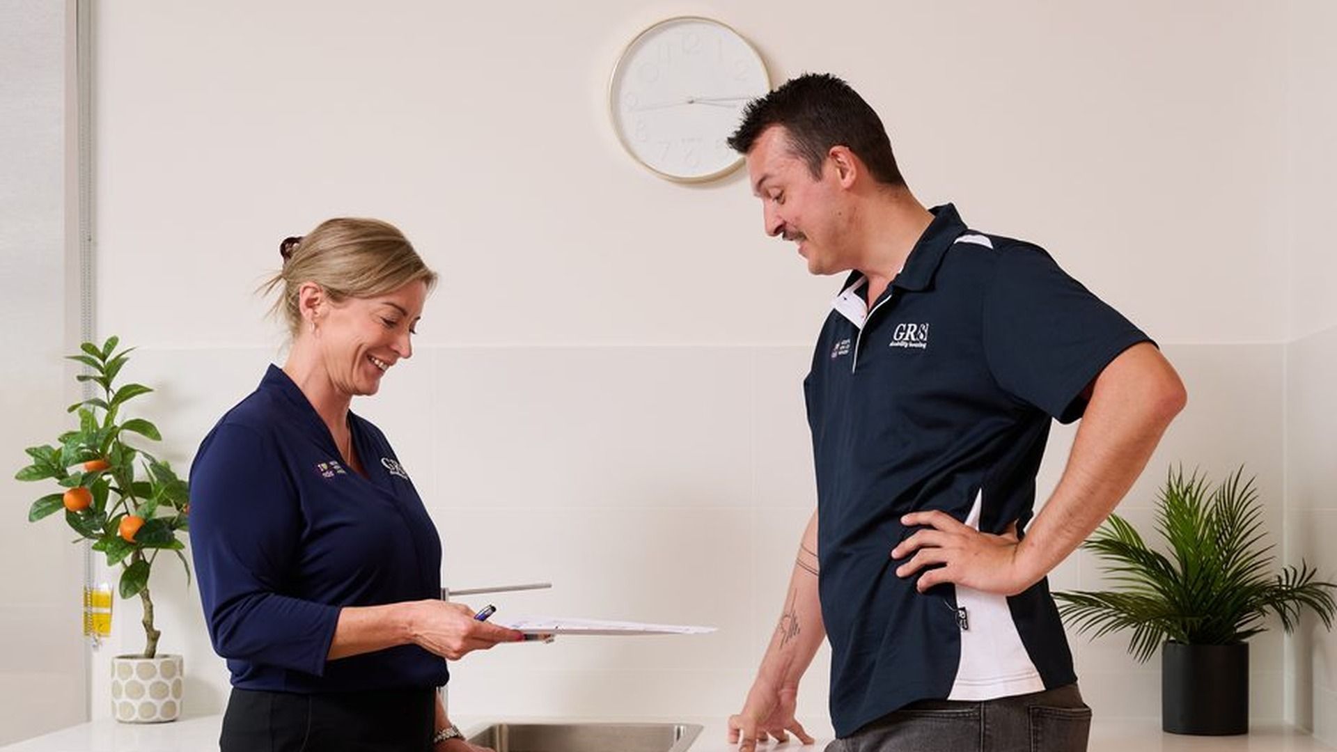 Two GR8 Disability Housing team members smiling and reviewing paperwork together at a bright, modern