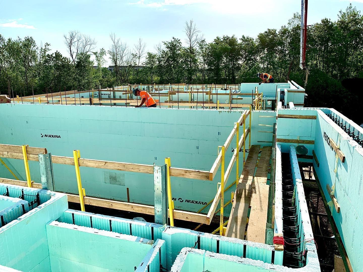 Construction site with blue ICF blocks and wooden supports; worker in orange vest.