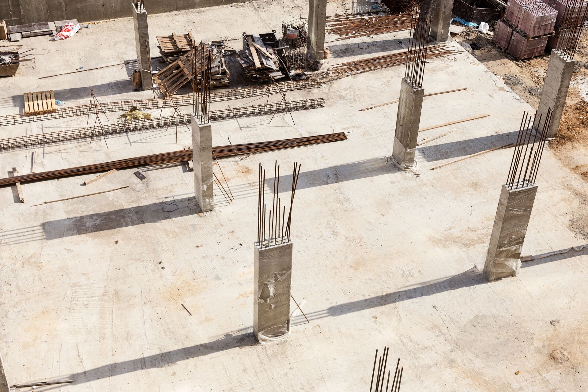 Construction site with concrete pillars and exposed rebar, unfinished concrete floor.
