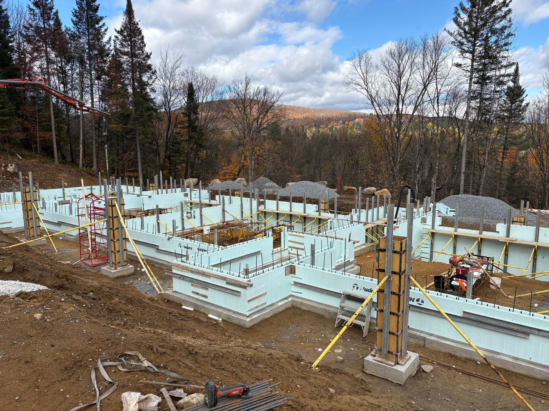 Construction site with insulated concrete form foundation, bracing, and surrounding trees under a cloudy sky.