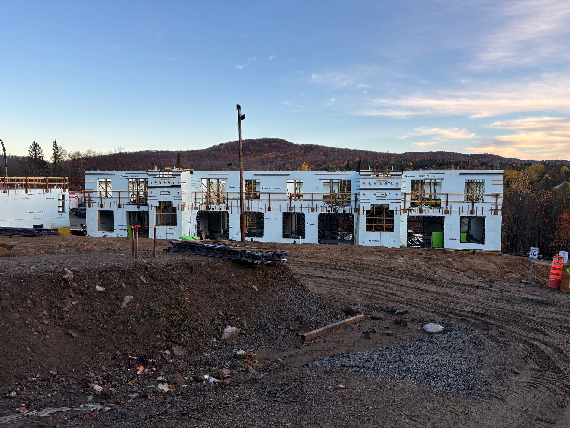 Construction site, several modular buildings under construction, white foam walls, dirt foreground, distant trees.
