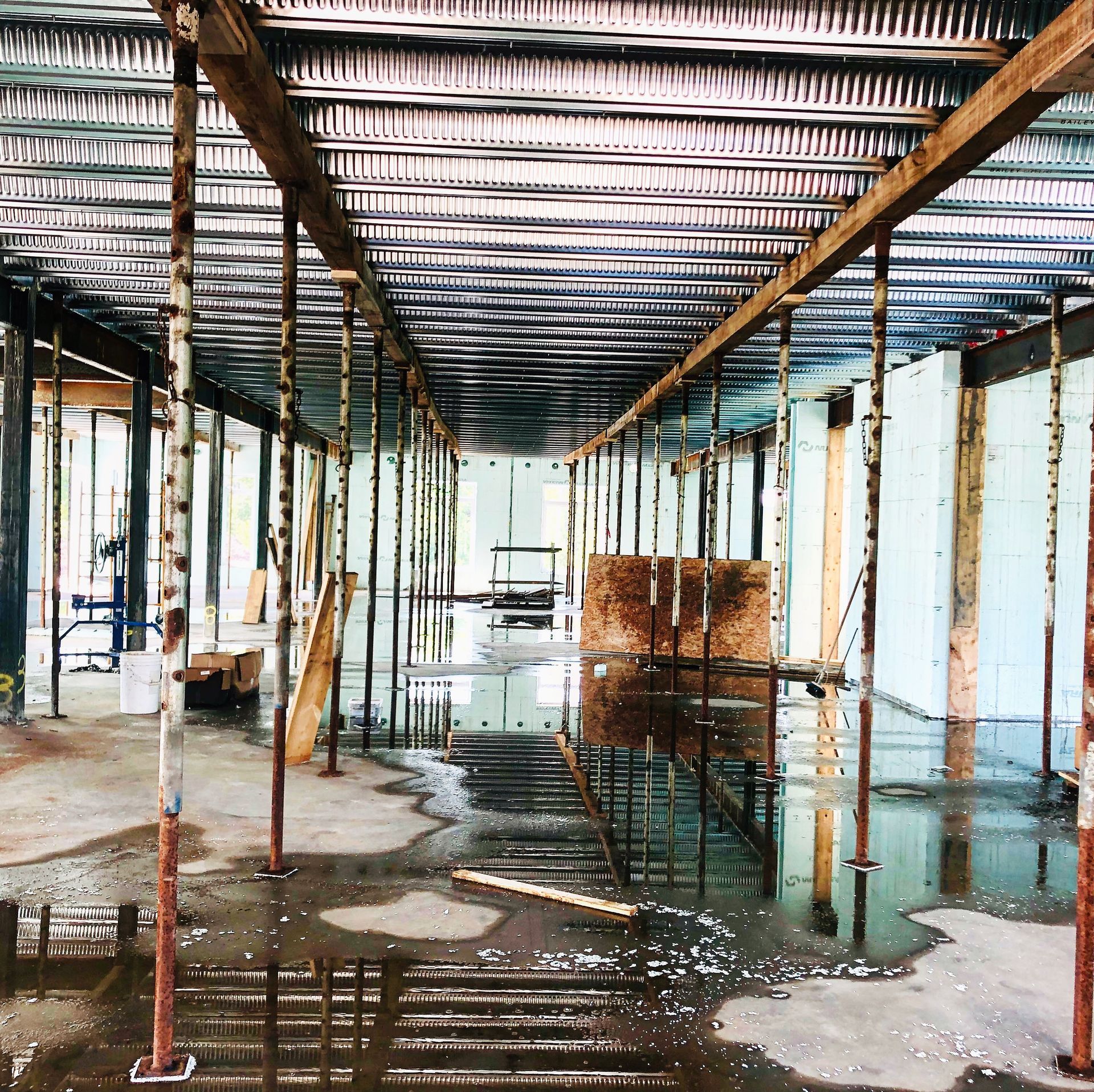 Interior of a construction site with supports, corrugated metal, and standing water on the floor.