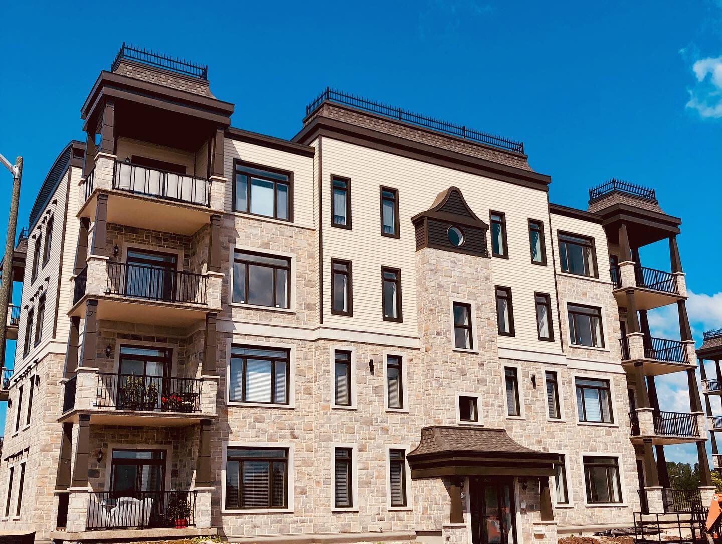 Multi-story building with stone and tan facade, balconies, and brown trim against a blue sky.