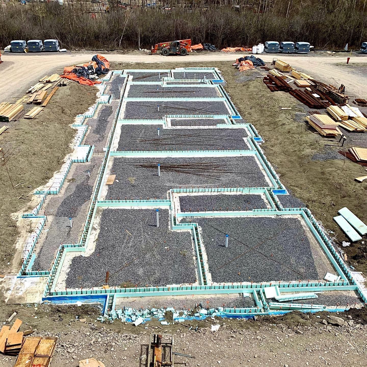 Construction site with concrete foundation walls framed in blue insulation, gravel infill.