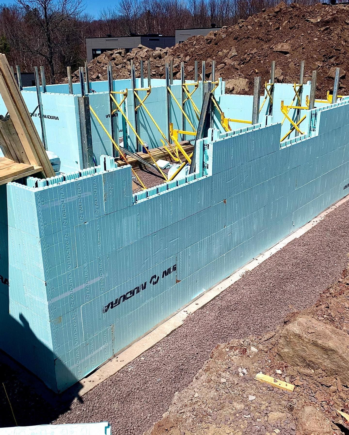 Blue insulated concrete form (ICF) foundation walls under construction, with bracing and gravel base.