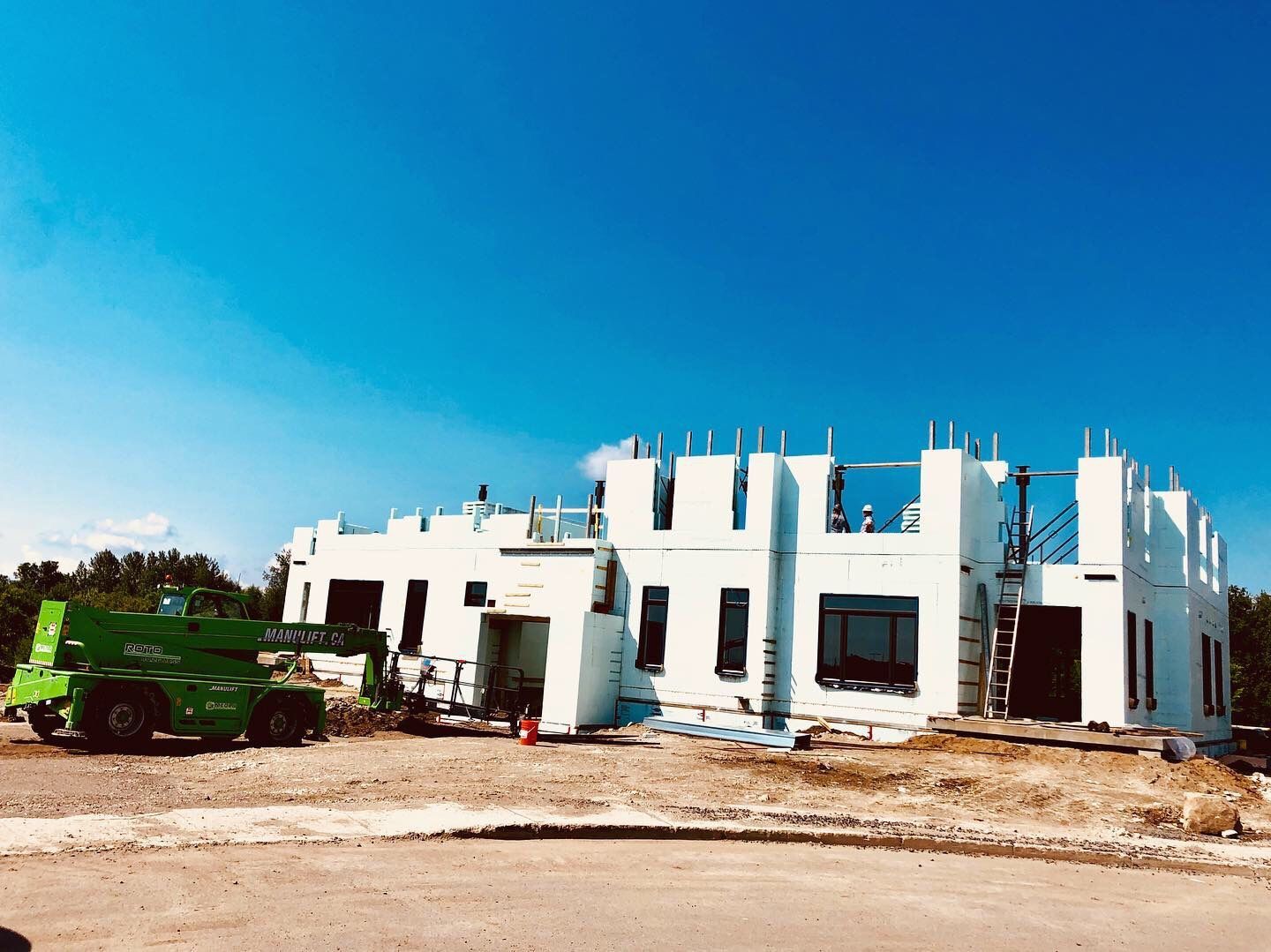 Building under construction with a green forklift on a sunny day.