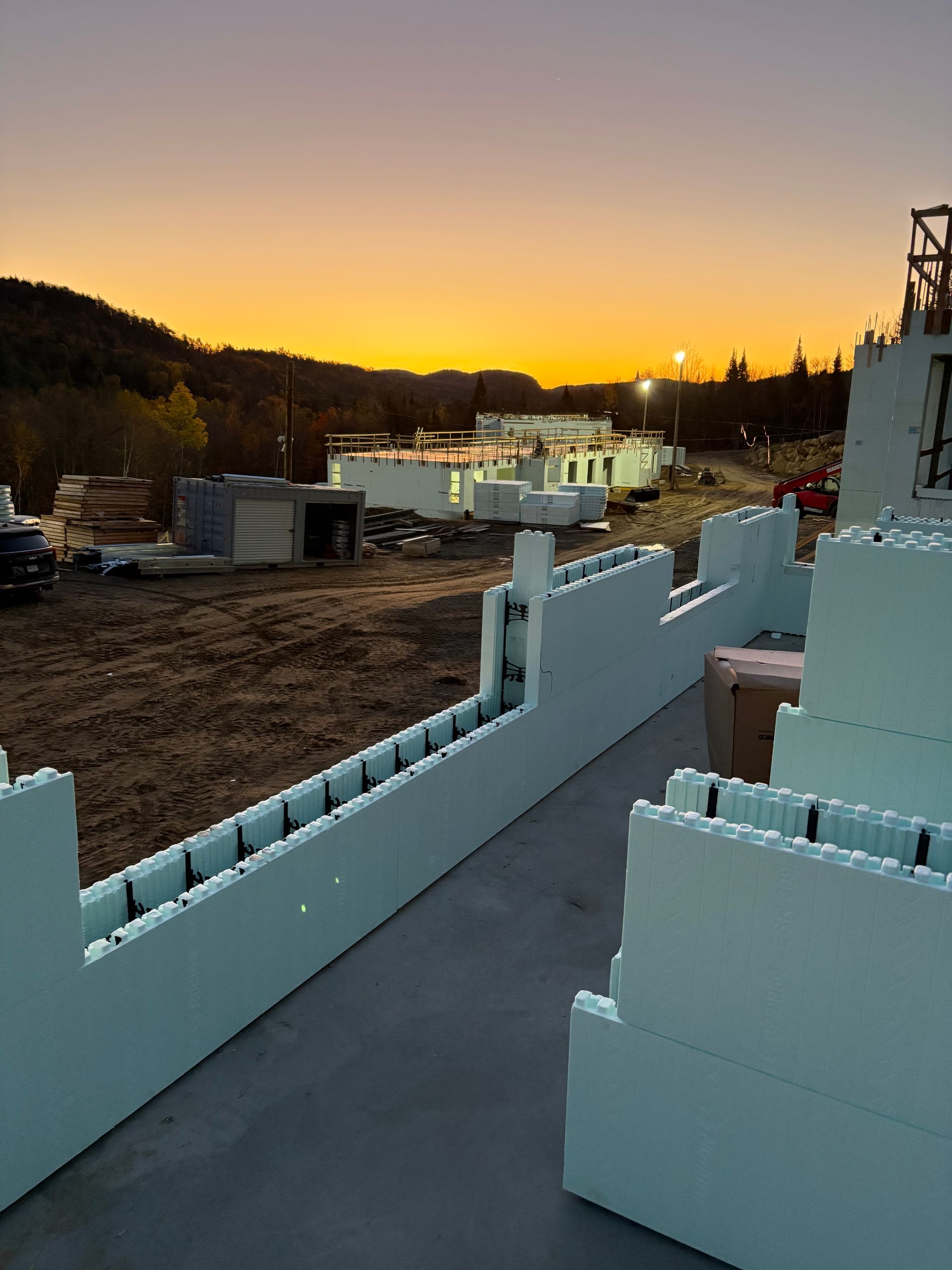 Construction site at dusk: Insulated concrete form walls, buildings, and a sunset.