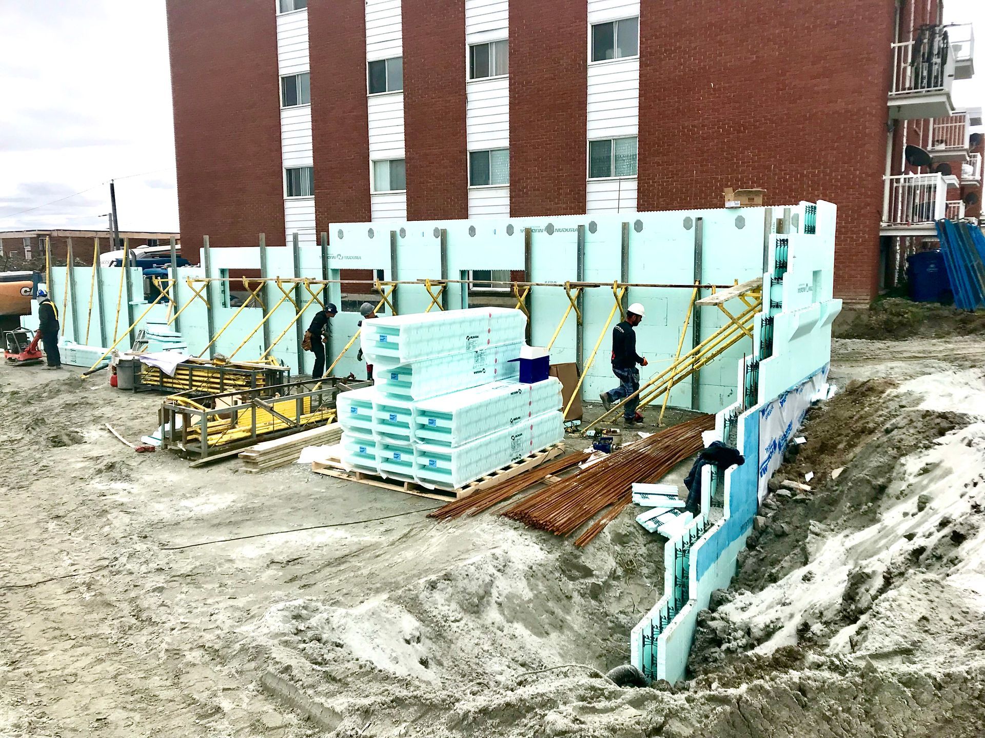 Construction site with workers building a wall using insulated concrete forms. Building in background.