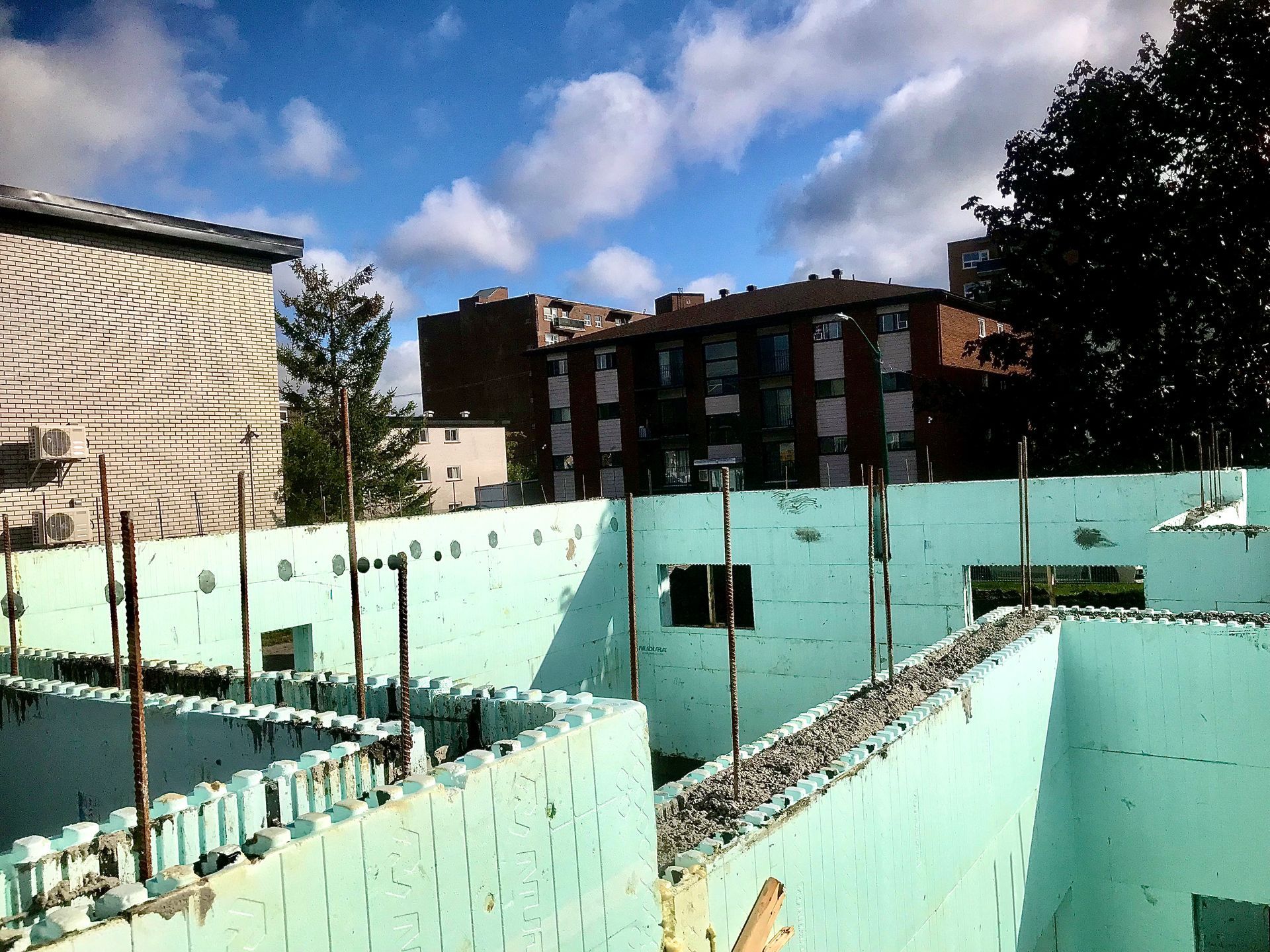Foundation construction site with turquoise insulated concrete forms, rebar, and buildings in the background.