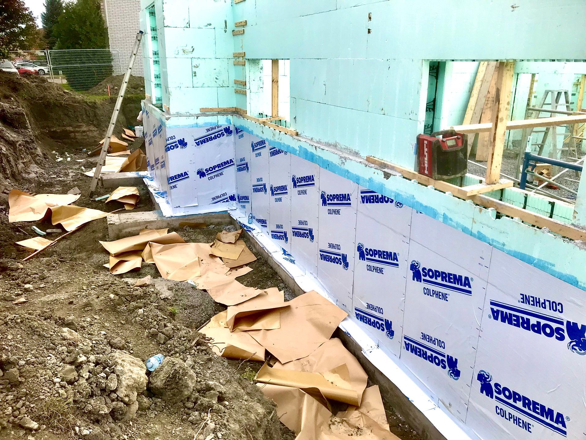 Construction site: Foundation walls covered in blue and white waterproofing membrane, with insulation panels.