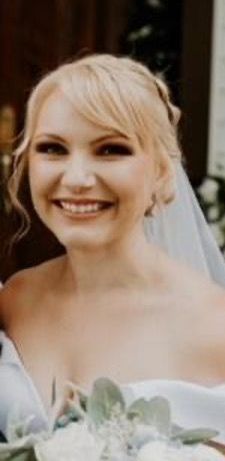 A woman in a wedding dress and veil is smiling and holding a bouquet of flowers.