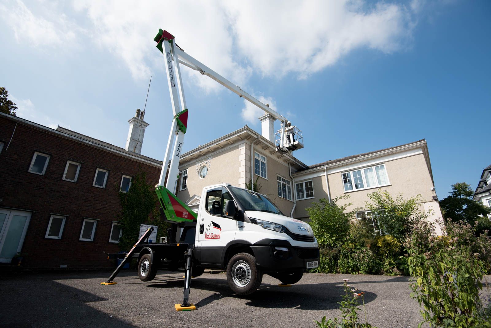 A white aerial lift truck with arm extended, working on a two-story building on a sunny day.