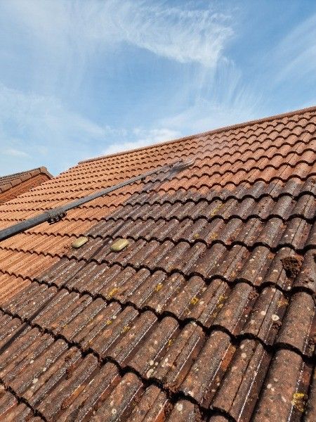 Cleaning a terracotta tile roof with a pressure washer; the right side is clean, the left side is dirty.