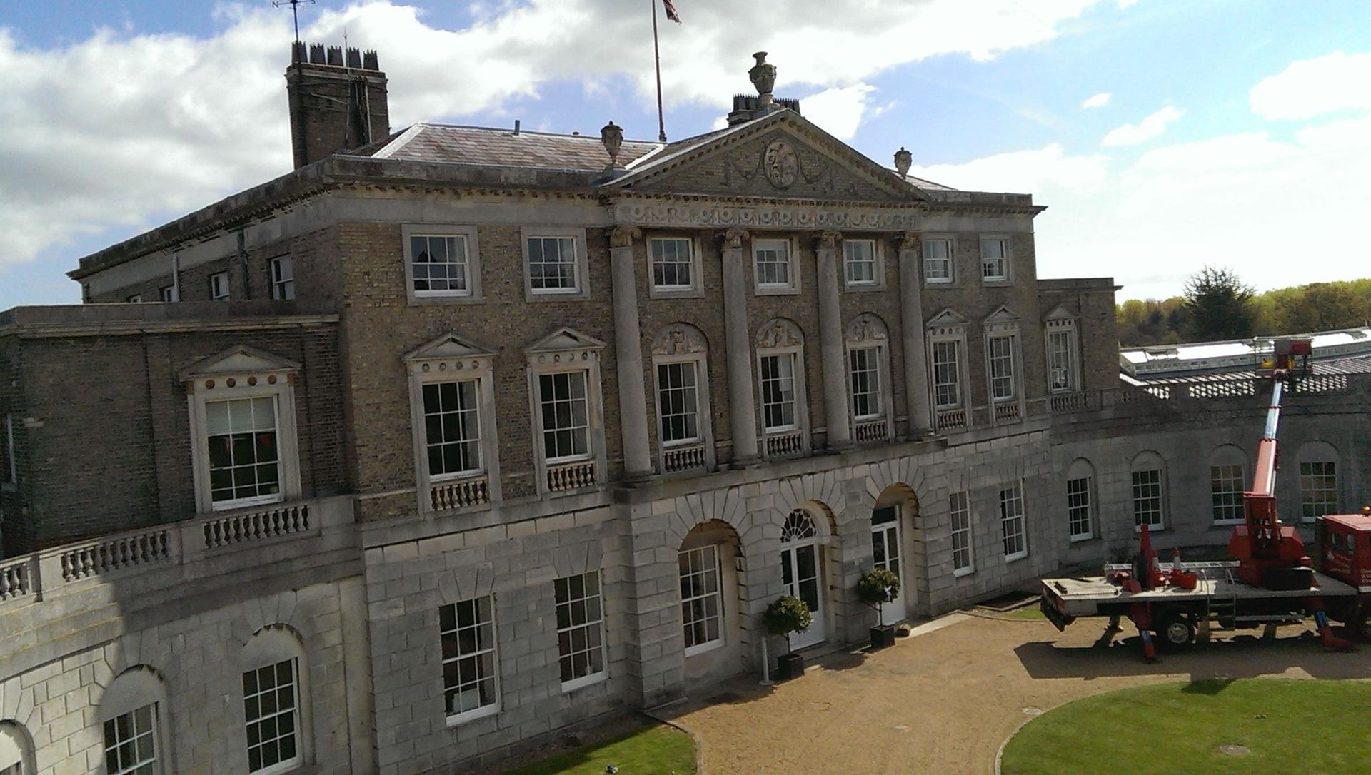 Stone mansion with columns and a flag on a sunny day. A crane truck is parked nearby.