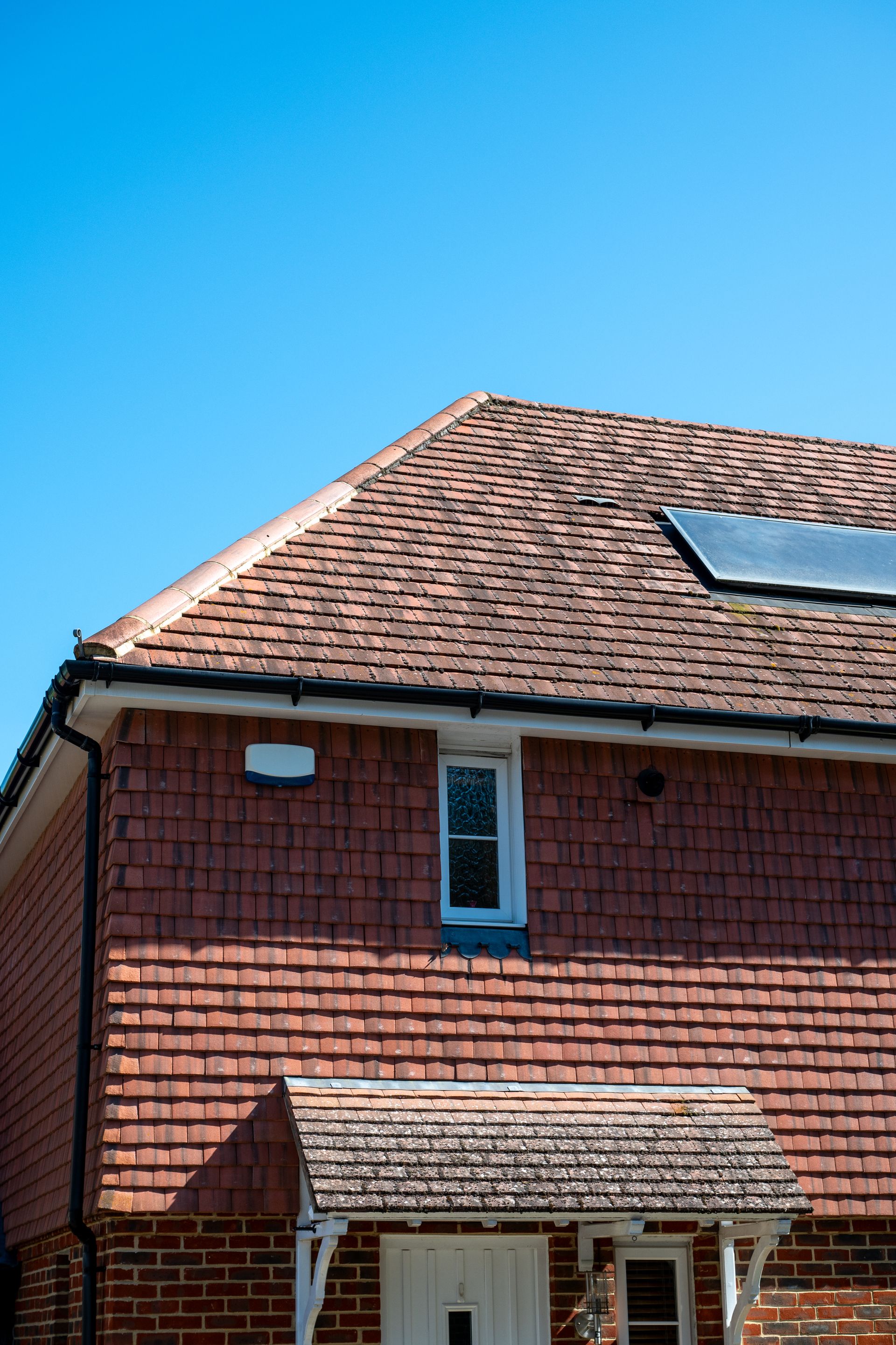 Red-tiled roof and brick facade of a house with a small window, against a bright blue sky.