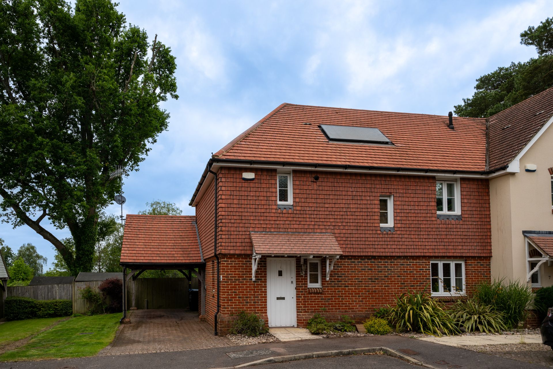 Brick house with a red tiled roof, white door, and carport, under a cloudy sky.