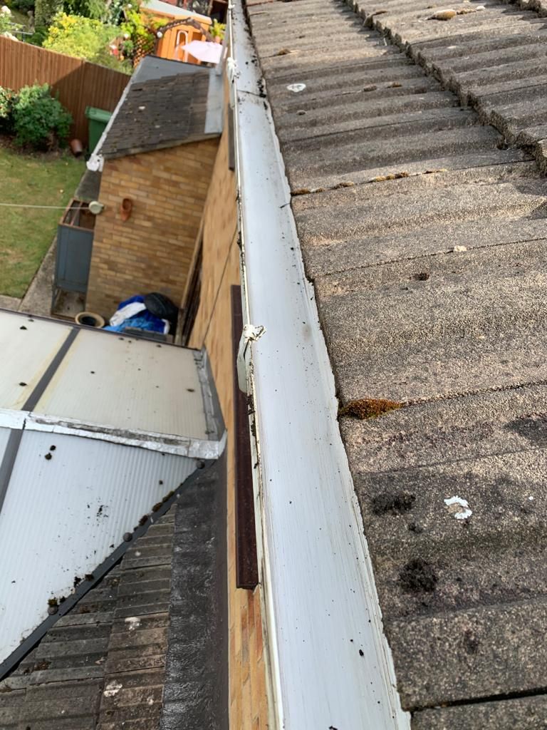 Rooftop view of gutter alongside brick building. Gray roof tiles and white gutter in a residential setting.